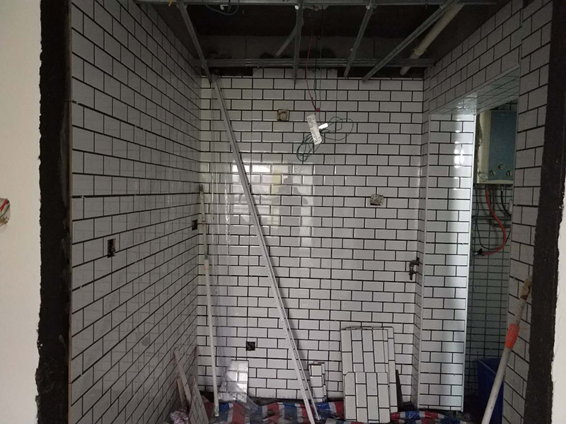 廁所裝修貼瓷磚案例：首先應(yīng)全部清理墻面上的各類(lèi)污物，打掃干凈現(xiàn)場(chǎng)，特別是腳落里；然后用泥刀先批墻，后用水泥漿找平。這個(gè)工序很重要，確保底子平，防止貼后空鼓；以及墻面要刷防水涂料，防止貼后浸水，一般高度不低于1.8米，刷的時(shí)候會(huì)稍高一些；接著把粘結(jié)劑漿料均勻的刮到墻上，記得瓷磚上墻將經(jīng)過(guò)預(yù)先清潔的瓷磚平整地鋪貼在粘結(jié)劑漿料基層上，使用橡膠錘將瓷磚拍實(shí)鋪平。施工過(guò)程中，可小幅度轉(zhuǎn)動(dòng)瓷磚，使?jié){料與瓷磚背面充分接觸。