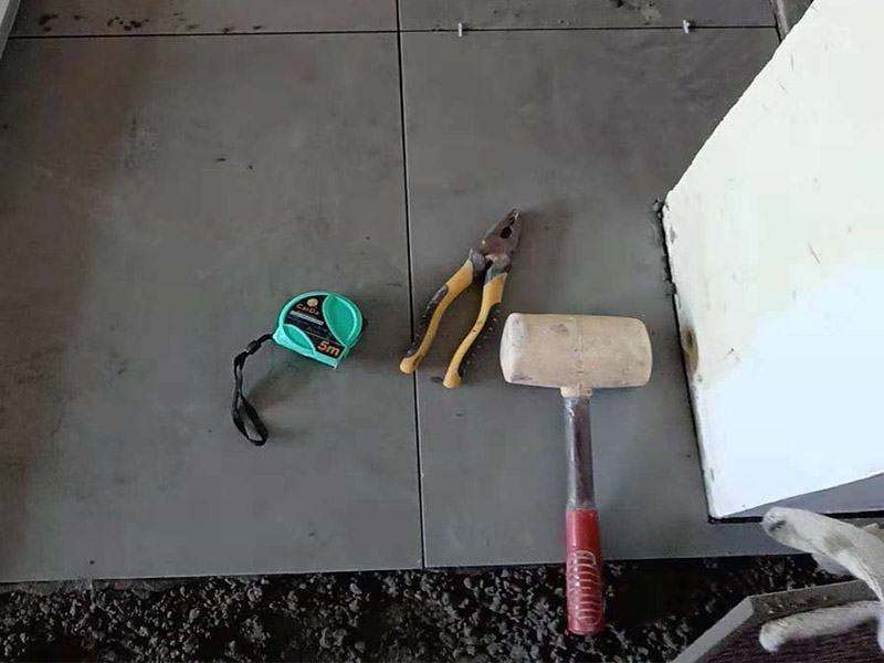 客廳地磚鋪貼：鋪貼的工具包括橡膠錘和粘結(jié)劑。在進(jìn)行施工之前先把所需要的這些材料都整理好放在一旁備用；基層的處理工作對(duì)瓷磚的平整度有很大的影響，對(duì)于基層要做好清潔工作，還有找平工作。放樣：在進(jìn)行瓷磚的鋪貼工作之前還事先找好垂直線，這樣可以在鋪貼的時(shí)候找到瓷磚的水平線，讓瓷磚鋪貼的更加的平整。粘結(jié)劑加水?dāng)嚢杈鶆?，靜置10分鐘之后就可以使用。將瓷磚表面的浮灰清除，再在瓷磚背面均勻的涂抹上粘結(jié)劑，按照預(yù)鋪的順序?qū)⒋纱u鋪貼在地面上，最后用橡膠錘輕輕拍打至服帖齊整。