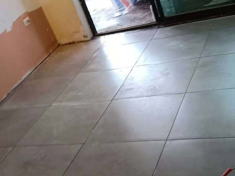 客廳地磚鋪貼：鋪貼的工具包括橡膠錘和粘結(jié)劑。在進(jìn)行施工之前先把所需要的這些材料都整理好放在一旁備用；基層的處理工作對(duì)瓷磚的平整度有很大的影響，對(duì)于基層要做好清潔工作，還有找平工作。放樣：在進(jìn)行瓷磚的鋪貼工作之前還事先找好垂直線，這樣可以在鋪貼的時(shí)候找到瓷磚的水平線，讓瓷磚鋪貼的更加的平整。粘結(jié)劑加水?dāng)嚢杈鶆?，靜置10分鐘之后就可以使用。將瓷磚表面的浮灰清除，再在瓷磚背面均勻的涂抹上粘結(jié)劑，按照預(yù)鋪的順序?qū)⒋纱u鋪貼在地面上，最后用橡膠錘輕輕拍打至服帖齊整。