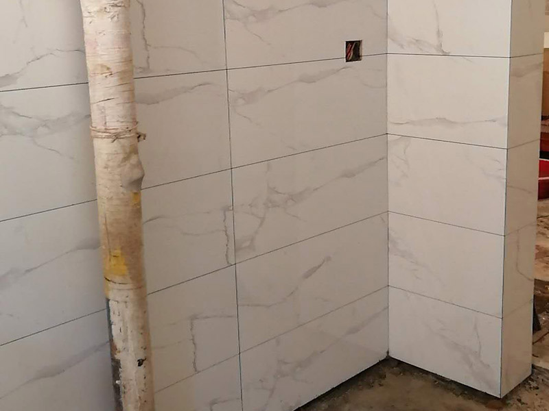 衛(wèi)生間瓷磚鋪貼：基層處理：首先應(yīng)除去基層表面的污垢，油漬，浮灰;除去基層上所有涂料層，膩?zhàn)訉?如果基層未能達(dá)到平整度要求，需對(duì)基層進(jìn)行預(yù)先的找平處理。  放樣：鋪貼瓷磚前需事先找好垂直線，以此為基準(zhǔn)鋪貼的瓷磚高低均勻、垂直美觀;此外，施工前在墻體四周需彈出標(biāo)高控制線，在地面彈出十字線，以控制地磚分隔尺寸。  預(yù)鋪：首先應(yīng)對(duì)瓷磚的色彩、紋理、表面平整等進(jìn)行嚴(yán)格的挑選，然后按照?qǐng)D紙要求預(yù)鋪。 調(diào)制粘結(jié)劑：加水后將粘結(jié)劑漿料攪拌至潤(rùn)滑均勻，無(wú)明顯塊狀或糊狀結(jié)塊，攪拌后的漿料靜置5-10分鐘后再稍加攪拌1-2分鐘即可使用。在開(kāi)始鋪貼施工前，需要先清理瓷磚表面的浮灰，污垢等。  抹漿料：將調(diào)制好的漿料均勻地抹在瓷磚背面，要求漿料飽滿。將瓷磚平整地鋪貼在基層上，使用橡膠錘將瓷磚拍實(shí)鋪平。施工過(guò)程中，可小幅度轉(zhuǎn)動(dòng)瓷磚，使?jié){料與瓷磚背面充分接觸。 瓷磚鋪貼結(jié)束后24小時(shí)，可進(jìn)行嵌縫施工。將調(diào)制好的嵌縫劑均勻地涂在磚與磚的縫隙內(nèi)。嵌縫后用浸濕的織物清理多余的嵌縫劑，保持瓷磚表面清潔。