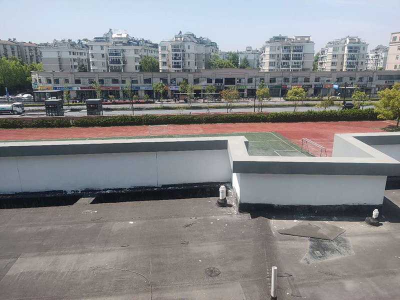 學(xué)校屋頂防水：屋頂做防水前，要先對需要防水施工的屋頂基層進行清潔，因為很多防水施工中要避免一些雜物、塵土等，打掃干凈了更有利于防水施工效果。屋頂防水施工就與室內(nèi)防水施工差不多，室內(nèi)的地漏、水管位置等都要重點涂刷，而屋頂中的水落口、女兒墻、檐口、陰陽角等位置也要先進行針對性的施工，也被稱為附加層施工。屋頂施工防水需要不少材料，特別是防水用的改性瀝青卷材、防水涂料等等，先對基層鋪貼一層防水卷材，其厚度要符合要求，尺寸根據(jù)屋頂面積進行裁剪。卷材一般歐式用熱熔的方式來鋪貼，也就是需要借助火焰噴槍來加熱進行滾鋪、粘貼，卷材從檐口處與屋脊平行的方向由下而上進行鋪貼。卷材的各個搭接處都要用噴槍來加熱粘結(jié)牢固，并且在邊緣末端收頭處要用密封膏來嵌填嚴密好才行。卷材鋪貼好后，要再一次進行屋頂清潔，保障干凈、干燥的施工環(huán)境，這時候就可以進行第一層的防水涂料刷涂了，第一遍一定要涂滿，不能出現(xiàn)遺漏、裂紋、氣泡、黏合不牢固等現(xiàn)象。