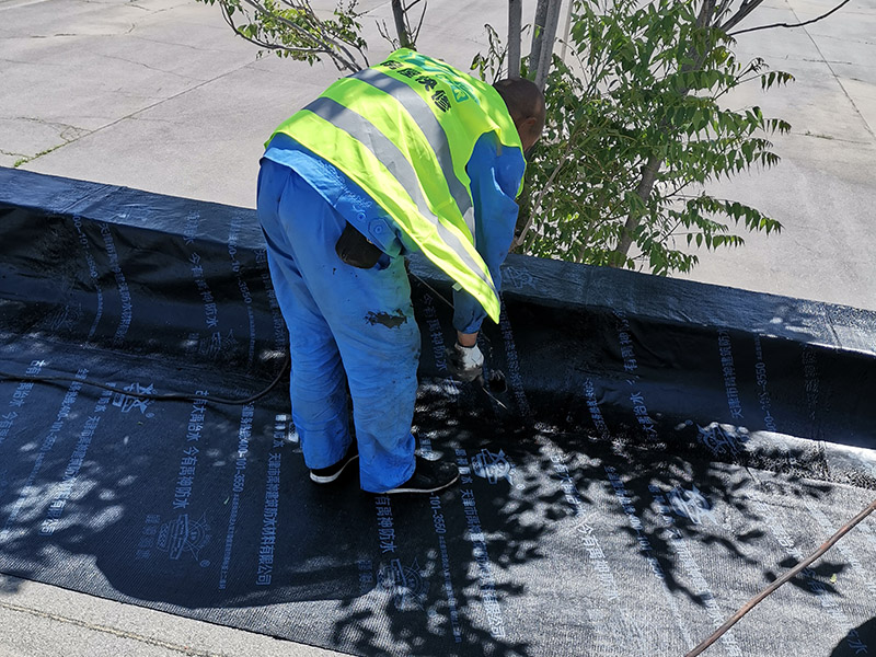 屋頂防水卷材鋪貼:清除基層表面雜物、油污、砂子，凸出表面的石子、砂漿疙瘩等應(yīng)清理干凈，清掃工作必須在施工中隨時進(jìn)行，并修補(bǔ)平整表面。尤其鏟除排水口、煙囪、管壁上的水泥砂漿等附著物；根據(jù)施工現(xiàn)場狀況，進(jìn)行合理定位，確定卷材鋪貼方向，在基層上彈好卷材控制線，依循流水方向從低往高進(jìn)行卷材試鋪。卷材試鋪后，先將要鋪貼的卷材剪好，反鋪于基面上(即是底部隔離紙朝上)，撕剝?nèi)ゾ聿母綦x紙。撕剝時，已剝開的隔離紙宜與粘結(jié)面保持45～60度的銳角，防止拉斷隔離紙，盡量保持在自然松弛狀態(tài)，但不要有皺折。