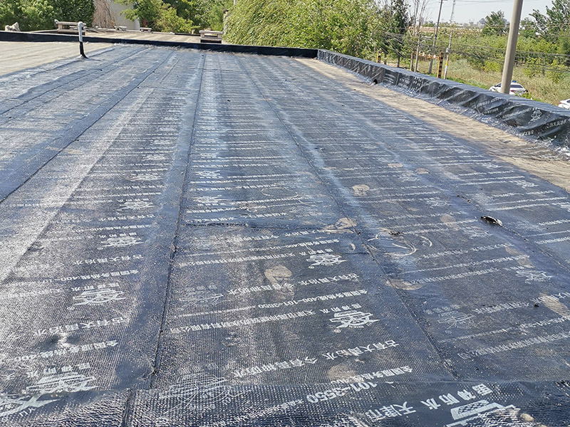 屋頂防水卷材鋪貼:清除基層表面雜物、油污、砂子，凸出表面的石子、砂漿疙瘩等應(yīng)清理干凈，清掃工作必須在施工中隨時進(jìn)行，并修補(bǔ)平整表面。尤其鏟除排水口、煙囪、管壁上的水泥砂漿等附著物；根據(jù)施工現(xiàn)場狀況，進(jìn)行合理定位，確定卷材鋪貼方向，在基層上彈好卷材控制線，依循流水方向從低往高進(jìn)行卷材試鋪。卷材試鋪后，先將要鋪貼的卷材剪好，反鋪于基面上(即是底部隔離紙朝上)，撕剝?nèi)ゾ聿母綦x紙。撕剝時，已剝開的隔離紙宜與粘結(jié)面保持45～60度的銳角，防止拉斷隔離紙，盡量保持在自然松弛狀態(tài)，但不要有皺折。