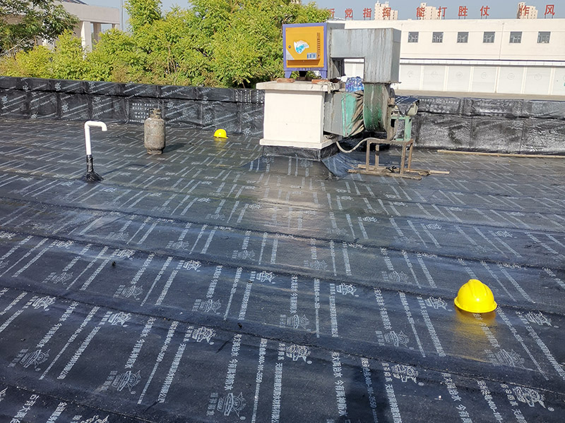 屋頂防水卷材鋪貼:清除基層表面雜物、油污、砂子，凸出表面的石子、砂漿疙瘩等應(yīng)清理干凈，清掃工作必須在施工中隨時進(jìn)行，并修補(bǔ)平整表面。尤其鏟除排水口、煙囪、管壁上的水泥砂漿等附著物；根據(jù)施工現(xiàn)場狀況，進(jìn)行合理定位，確定卷材鋪貼方向，在基層上彈好卷材控制線，依循流水方向從低往高進(jìn)行卷材試鋪。卷材試鋪后，先將要鋪貼的卷材剪好，反鋪于基面上(即是底部隔離紙朝上)，撕剝?nèi)ゾ聿母綦x紙。撕剝時，已剝開的隔離紙宜與粘結(jié)面保持45～60度的銳角，防止拉斷隔離紙，盡量保持在自然松弛狀態(tài)，但不要有皺折。