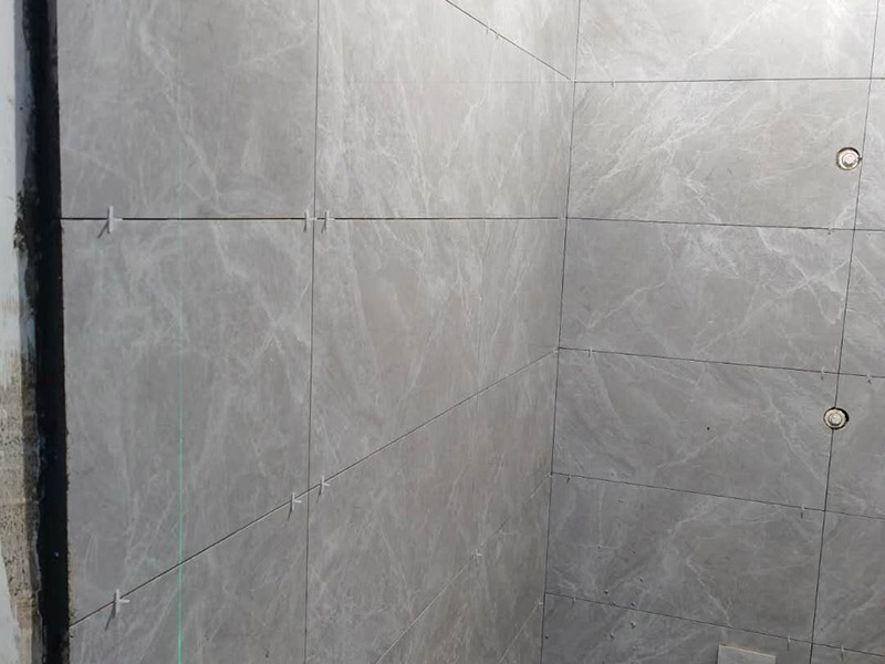 衛(wèi)生間貼磚施工：應(yīng)全部清理墻面上的各類污物，打掃干凈現(xiàn)場，特別是腳落里。用泥刀先批墻，后用水泥漿找平。這個工序很重要，確保底子平，防止貼后空鼓。墻面要刷防水涂料，防止貼后浸水，一般高度不低于1.8米，刷的時候會稍高一些。根據(jù)設(shè)計鋪貼圖樣的要求，確定排磚方案，用墨斗彈線，以減少施工損耗。把剛剛攪拌好的粘結(jié)劑漿料均勻的刮到墻上。瓷磚上墻將經(jīng)過預(yù)先清潔的瓷磚平整地鋪貼在粘結(jié)劑漿料基層上，使用橡膠錘將瓷磚拍實鋪平。施工過程中，可小幅度轉(zhuǎn)動瓷磚，使?jié){料與瓷磚背面充分接觸。專家建議在鋪貼時，隨機取下已鋪貼于基層上的瓷磚作檢查。確保漿料與瓷磚背面的充分接觸。 留縫大小調(diào)整根據(jù)瓷磚的尺寸，在磚與磚之間預(yù)留相應(yīng)尺寸的縫隙留待嵌縫。可用牙簽等先固定，粘結(jié)劑具有一定的可調(diào)整性，可對留縫的大小進(jìn)行調(diào)整。