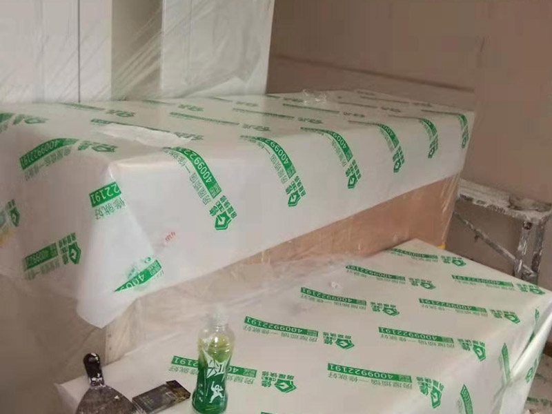 全屋家具成品保護：滿鋪成品瓦楞紙板，再用干凈彩條布滿鋪在普通石膏板上，在彩條布交接處及轉(zhuǎn)角處用膠帶固定，也可選用木芯板或三夾板。材料選用視上人、車情況而定。 所有成品飾面板在安裝好后必須用PE保護膜覆蓋包起來，所有成品飾面板的陽角位必須用硬質(zhì)紙護角或泡沫棉進行保護性包裝，防止交被其他施工人員碰撞。 1、入戶門扇用公司統(tǒng)一的門貼進行全面包裹保護，用透明膠帶將保護膜粘貼牢固平整。 2、用標準保護膜將門框三面保護完整并固定牢固。 3、工程完工后拆除保護膜時如果有粘貼時的膠痕，應用酒精或?qū)Ｓ玫那逦蹌┣宄z痕。