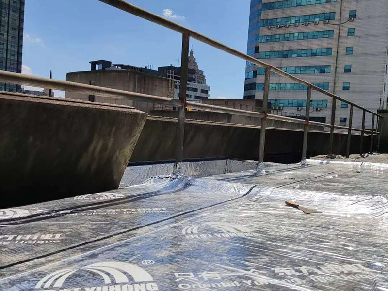 屋頂防水卷材鋪貼:1、由于設(shè)計(jì)要求屋面找坡層按2％坡度放坡，因此卷材鋪設(shè)時(shí)應(yīng)平行于屋脊自下而上的鋪貼，卷材搭縫必須嚴(yán)密，縫口應(yīng)順?biāo)鞣较虼罱?，其寬度不?yīng)小于50mm，上下屋接縫應(yīng)左右錯(cuò)開(kāi)250mm，在鋪大面積防水卷材之前，應(yīng)將檐溝，管道口、雨水口處的附加防水布鋪好后由屋頂?shù)牡吞幭蚋咛庍M(jìn)行大面積的鋪貼。 2、屋頂卷材遇到女兒墻時(shí)，應(yīng)將卷材沿墻上卷，高度應(yīng)低于250mm，然后固定在墻上預(yù)埋的木磚和木塊上，并用1：3水泥砂漿做坡水。 3、凡管道等伸出屋面的構(gòu)件必須在屋頂上開(kāi)孔時(shí)，為了防漏水應(yīng)將卷材向上翻起，抹以水泥砂漿或再蓋上鍍鋅鐵皮起擋水作用，泛水高度不超過(guò)200mm。 防水材料卷材層應(yīng)粘結(jié)牢固，無(wú)空鼓、損傷、滑移，翹邊、起泡、皺折等缺陷。防水工程施工完畢后，必須作蓄水試驗(yàn)合格后開(kāi)始進(jìn)行下道工序。