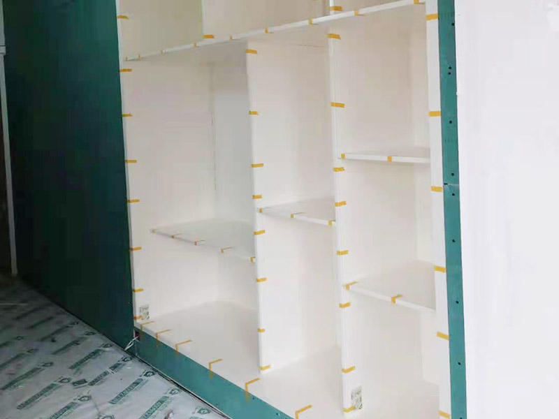 客廳定制柜體安裝：用墊布點好地板，先從靠墻的一端寬側(cè)板開始組裝，將寬側(cè)板平放于地面上（離后墻面保持700mm間隔）。首先將填好的三合一膠塞的板件，平放在墊布上，檢查孔距與圖紙相符，并裝上三合一單連桿。然后將固層釘上木塞，固定于寬側(cè)板上面，頂板大柄孔朝上，其余固層都朝下，腳線大柄孔朝內(nèi)（中間固層與L架高度一致，即底板到固層內(nèi)空為960mm，現(xiàn)場打?qū)影蹇祝?。放上?cè)板，釘上木塞，木塞要求連通兩邊的固層。在第二個柜固層上面裝好雙連桿，留意雙連桿上面大柄只能鎖住一半，即90&deg;。當(dāng)兩件固層與側(cè)板固定后再同時擰緊大柄。裝第三個柜時重復(fù)第二個柜的安裝步驟。